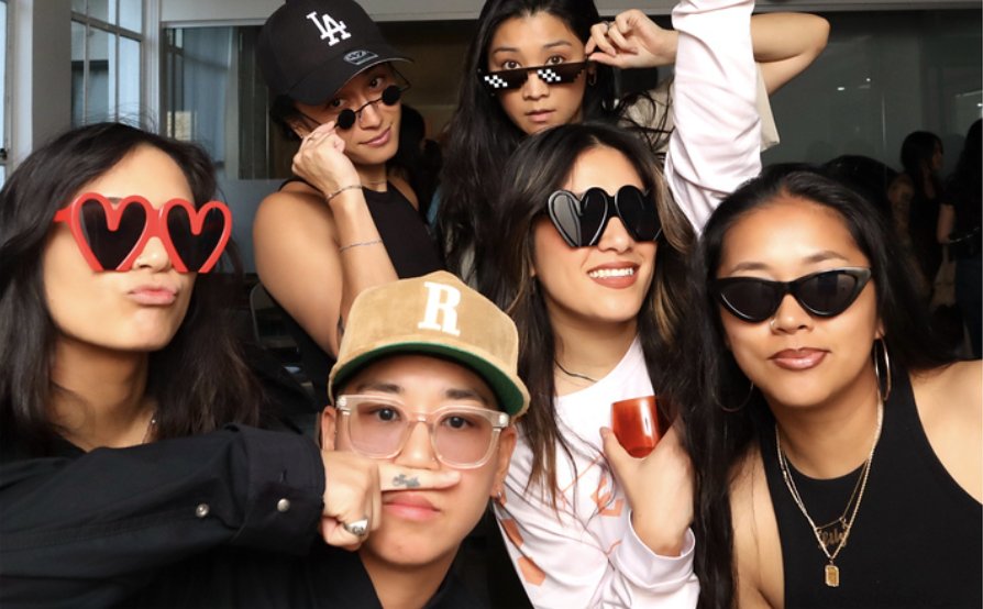 Group of friends posing with heart-shaped sunglasses, pixel shades and peace signs at a Mighty Little Studio activation